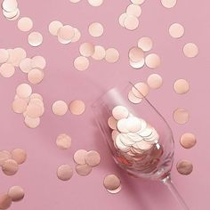 a glass filled with lots of coins on top of a pink table covered in confetti