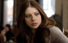 a woman with long brown hair and blue eyes looks at the camera while sitting down