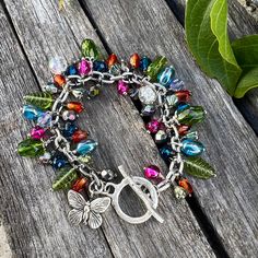 "This gorgeous one-of-a-kind floral inspired bracelet features a myriad of stunning Czech glass beads and vintage glass beads in a variety of shapes, sizes and finishes including flowers, leaves, teardrops and more along with a beautiful antique silver butterfly and botanical toggle clasp to complete the look. All 54 beads have been individually and meticulously wire wrapped by hand onto a textured antique silver stainless steel oval chain. Bracelet measures 7.5\" in length but feel free to message me if you need a different size and I'll be happy to adjust it for you. 😊 Add some sparkle to your wardrobe with this botanical beauty. It looks stunning with everything from jeans to dresses and also makes a wonderful and thoughtful gift for that someone special!" Bohemian Crystal Beaded Bracelets For Jewelry Making, Bohemian Silver Czech Glass Jewelry, Bohemian Czech Glass Silver Jewelry, Bohemian Multicolor Metal Charm Bracelet, Bohemian Style Multicolor Metal Charm Bracelet, Multicolor Beaded Metal Charm Bracelet, Bohemian Multicolor Nickel-free Charm Bracelet, Silver Bracelet With Colorful Glass Beads, Whimsical Silver Glass Jewelry