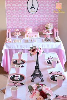 the table is set with pink and white plates, cups, and napkins in front of the eiffel tower