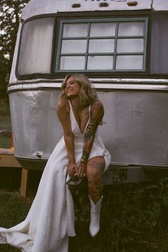 a woman sitting on the ground in front of an old camper with her legs crossed