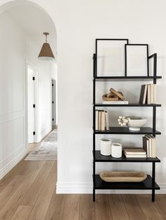 a shelf with books and other items on it in a white walled entryway area