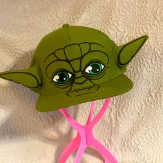 there is a green hat on top of a pink pair of hairbrushes with the face of yoda