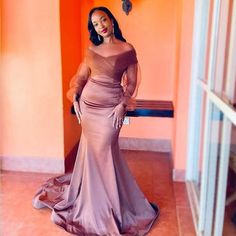 a woman standing in front of an orange wall wearing a long dress with sleeves on it