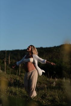 a pregnant woman standing in the grass with her arms spread out and looking up into the sky