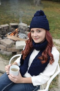 a woman sitting on a chair with a cup of coffee in front of an open fire pit