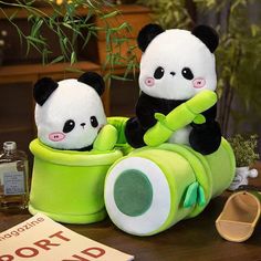 two stuffed panda bears sitting in a green toy car on a table next to a plant