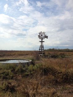 a windmill sitting in the middle of a field next to a small pond and grass