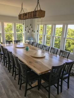 a large wooden table with chairs around it in front of two big windows that look out onto the woods