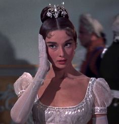 a woman wearing a tiara and holding her hand up to her face while standing in front of other people