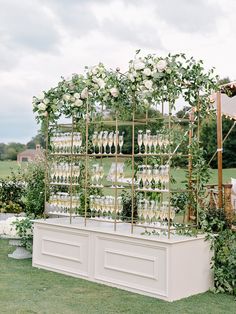 an outdoor bar with wine glasses and greenery on the top, surrounded by white flowers