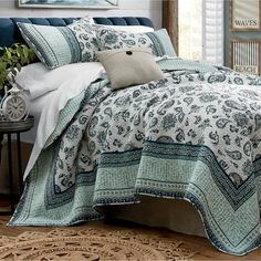 a bed with blue and white bedspread, pillows and blankets on top of it