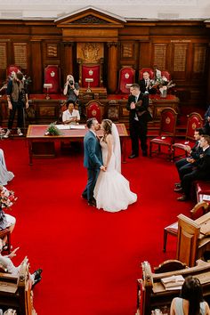 a bride and groom standing in front of a red carpeted ceremony room with people taking pictures