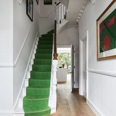 a green carpeted staircase leading up to a white wall with framed pictures on it