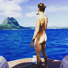 a man standing on top of a boat in the ocean next to another man with tattoos