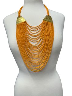 Add a touch of ethnic elegance to your outfit with this gorgeous long-beaded brass pendant necklace. The pendant is made of beads and features intricate brasswork in a beautiful shade of orange. The necklace is designed in an ethnic style, making it perfect for anyone who loves to add a unique touch to their look. The necklace is perfect for anyone who loves African-inspired jewellery and wants an authentic piece to add to their collection. The necklace would look stunning paired with a simple dress or top, adding colour to your outfit. Colour - Orange Length - 22inches Material: Beads, Brass Artisan Orange Beaded Necklaces For Festivals, Gold Beaded Long Necklace For Festival, Orange Beaded Necklaces For Festivals, Traditional Orange Beads For Festive Occasions, Gold Multi-strand Necklaces For Festivals, Gold Fair Trade Beaded Jewelry, Bohemian Gold Long Necklace With Round Beads, Bohemian Gold Beaded Long Necklace, Traditional Handmade Gold Long Necklace