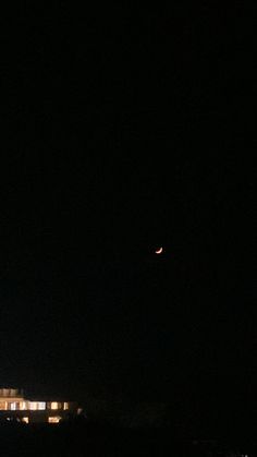 the moon is seen in the dark sky over a building at night with lights on