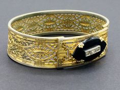 "Beautiful gold filigree bracelet made by Plainville Stock Company in the 1930s. The front panel features a black onyx ellipse set with rhinestones. This is a common theme for mourning jewelry, as it signified \"a light in the darkness\" and was intended to give comfort to the bereaved. I think the sentiment is meaningful even for those who have not lost a loved one, and can be a reminder of goals and important life motifs. CONDITION/SIZE: Good vintage condition - some finish loss which is reall Vintage Hand Set Yellow Gold Jewelry, Yellow Gold Filigree Bracelet For Formal Occasions, Vintage Hand Set Bracelets For Formal Occasions, Antique Yellow Gold Bracelets For Evening, Antique Yellow Gold Bracelet For Evening Wear, Art Deco Wedding Bracelets With Hand Set, Formal Cuff Bracelet With Intricate Design, Art Deco Wedding Bracelet With Hand Set, Gold Hinged Jewelry For Evening