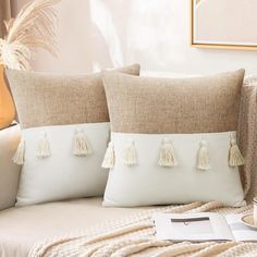 two pillows with tassels on them sitting on a couch next to a coffee cup