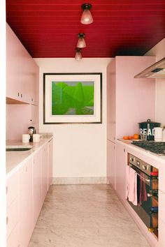 a kitchen with pink cabinets and white counter tops is seen in this image, there are two hanging lights above the stove