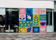 a colorful mural on the side of a building in front of a glass door with flowers and leaves painted on it