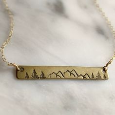 This brass bar necklace is a beautiful and unique piece of jewelry that captures the rugged beauty of the outdoors. Handmade in Colorado, the necklace features a 14k gold fill chain adding beauty and durability that will last. The brass bar pendant is stamped with a stunning design of mountains and pine trees. This necklace is perfect for anyone who loves the outdoors and wants to carry a piece of the mountains with them wherever they go. ● Solid Brass bar ● 14k Gold Fill 16” Chain ● Made by han Mountain Bar, Brass Bar, Outdoor Enthusiast, Bar Pendant, Pine Trees, Jewelry Inspo, Gold Filled Chain, Bar Necklace, The Outdoors