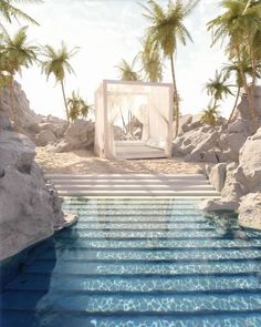 an outdoor pool surrounded by palm trees and rocks with a canopy bed in the middle