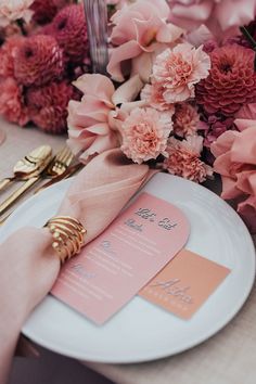 the table is set with pink flowers and gold place settings