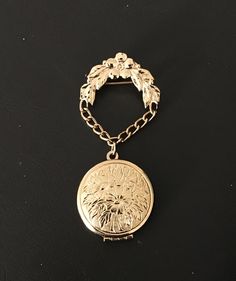 "Lovely vintage signed Monet hanging/dangling gold-tone brooch with impressed intricate floral design on the front and back of the locket, which hangs from a chain connected to a flower-and-leaf arch. (Any darker areas are reflections of us taking the photo! The pin has a polished finish.) The pin is in excellent condition and measures approx. 1.25\" across (arched pin at the top; the locket is 1\" across) and is 2.75\" long with the locket closed. See photo 3 to see the open locket; the hinge is at the base and the locket opens downward. This piece is as beautiful to wear as it would be in a collection.  We do our best to describe each selection and welcome any questions you may have. Pictures are also part of the description, so please look them over and read the entire description. Chec Antique Gold Medallion Brooch, Victorian Gold Brooch With Locket, Victorian Gold Locket Brooches, Victorian Gold Medallion Brooches, Victorian Gold Pendant Brooches, Gold Locket-shaped Brooch, Gold Locket Brooch For Collectors, Gold Pendant Locket Brooch, Gold Pendant Locket Brooches