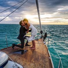 a man and woman kissing on the deck of a sailboat in the middle of the ocean