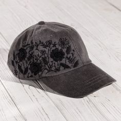 a gray hat with black flowers on it sitting on top of a white wooden floor