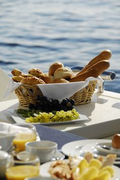 an assortment of breads and pastries on a table next to the ocean with water in the background