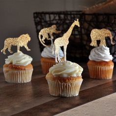 four cupcakes with gold giraffe toppers on them sitting on a table