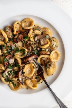 a white plate topped with pasta covered in mushrooms and parsley next to a fork