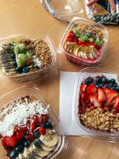 four plastic containers filled with fruit and granola on top of a wooden table,