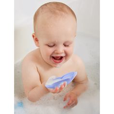 a smiling baby in a bathtub holding a blue toothbrush