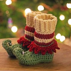 crocheted booties with red, white and green stripes on them sitting next to a christmas tree