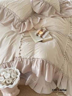 a bed with ruffled sheets and white flowers on the bottom edge, next to a candle