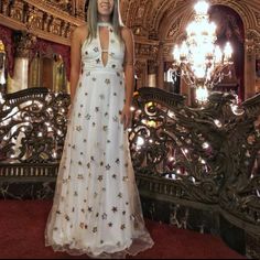 a woman wearing a white dress standing in front of a railing and chandelier