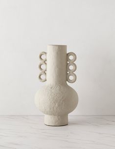 a large white vase sitting on top of a table next to a wall and floor