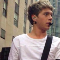 a young man with ear buds standing in front of a tall building and talking on his cell phone