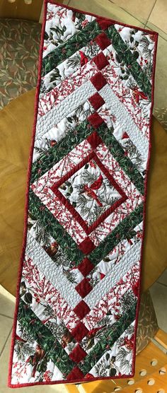 a quilted christmas table runner on top of a wooden chair with red and white trim