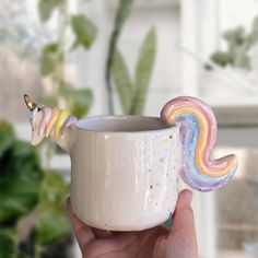 a hand holding a coffee cup with a rainbow unicorn horn on it