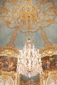 a chandelier hanging from the ceiling in a room with paintings on the walls