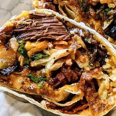 two tacos filled with meat and vegetables sitting on top of a white paper wrapper