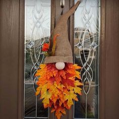 a scarecrow door hanger decorated with fall leaves and an orange flower on the front door