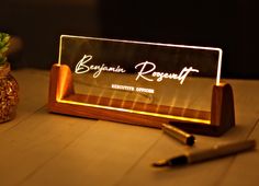 an illuminated business card holder with pen and plant next to it on a wooden table