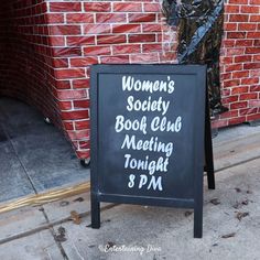 a woman's society book club meeting tonight 8 pm sign on the sidewalk in front of a brick building