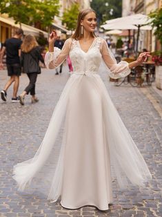 a woman in a white dress is standing on a cobblestone street with her arms outstretched