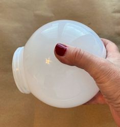 a woman's hand holding a white plastic bottle with red nail polish on it